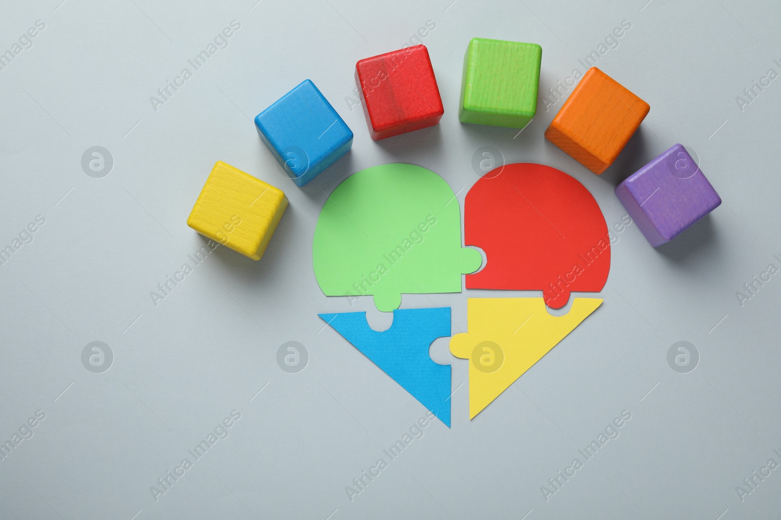 Photo of Colorful cubes and heart made of puzzle pieces on grey background, flat lay