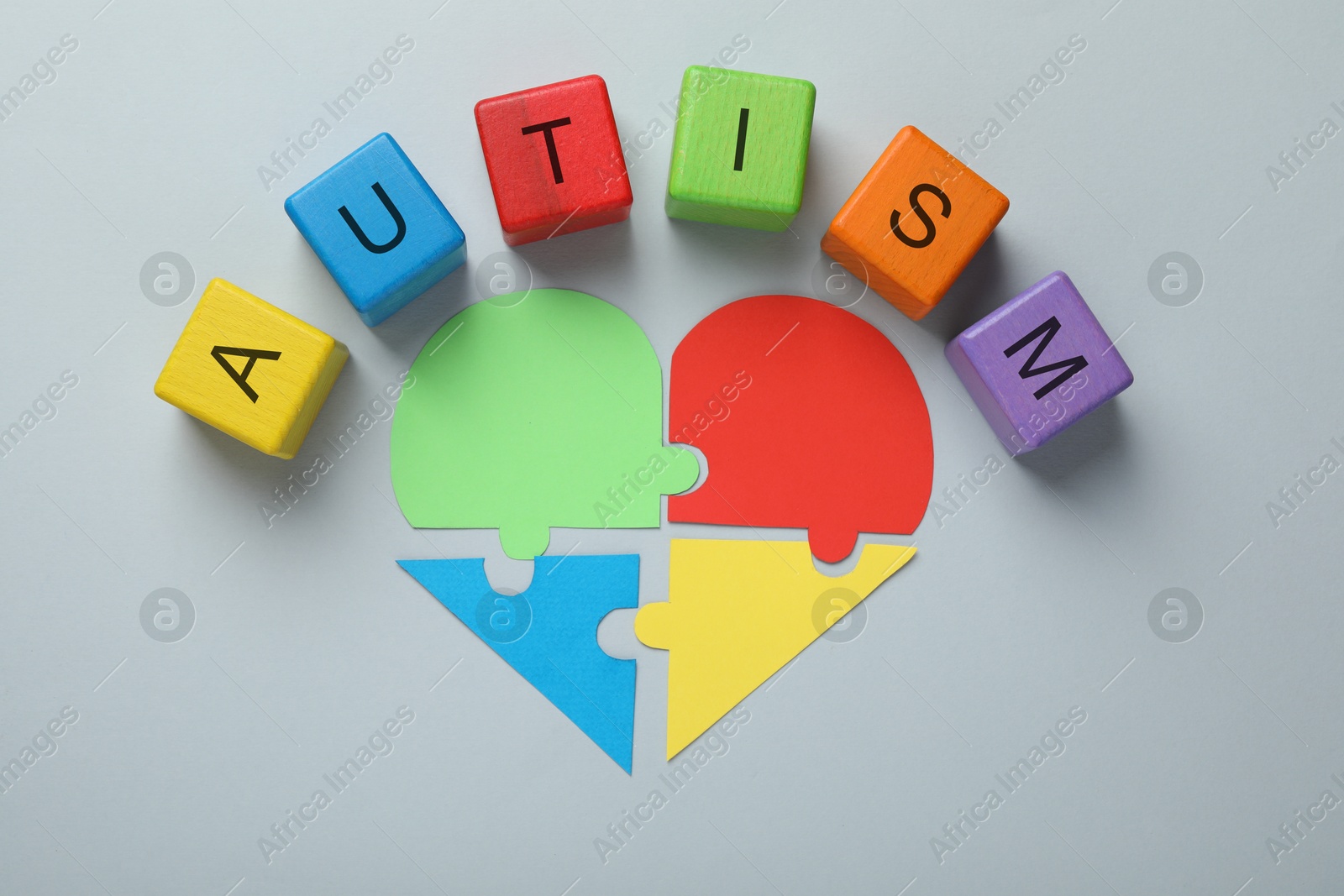 Photo of Colorful cubes with word Autism and heart made of puzzle pieces on grey background, flat lay