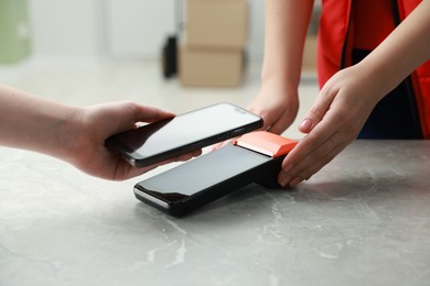 Photo of Woman paying for service with smartphone via terminal at table indoors, closeup