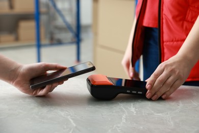 Photo of Woman paying for service with smartphone via terminal at table indoors, closeup