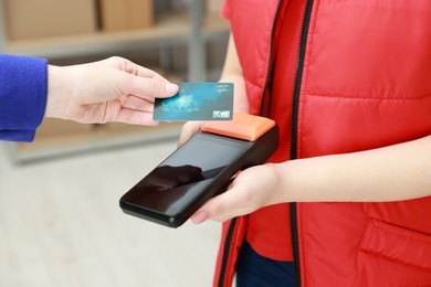 Photo of Woman paying for service with credit card via terminal indoors, closeup