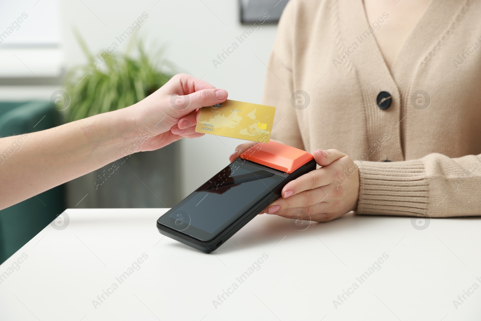 Photo of Woman paying for service with credit card via terminal at white table indoors, closeup