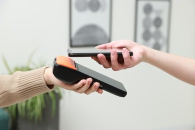 Photo of Woman paying for service with smartphone via terminal indoors, closeup