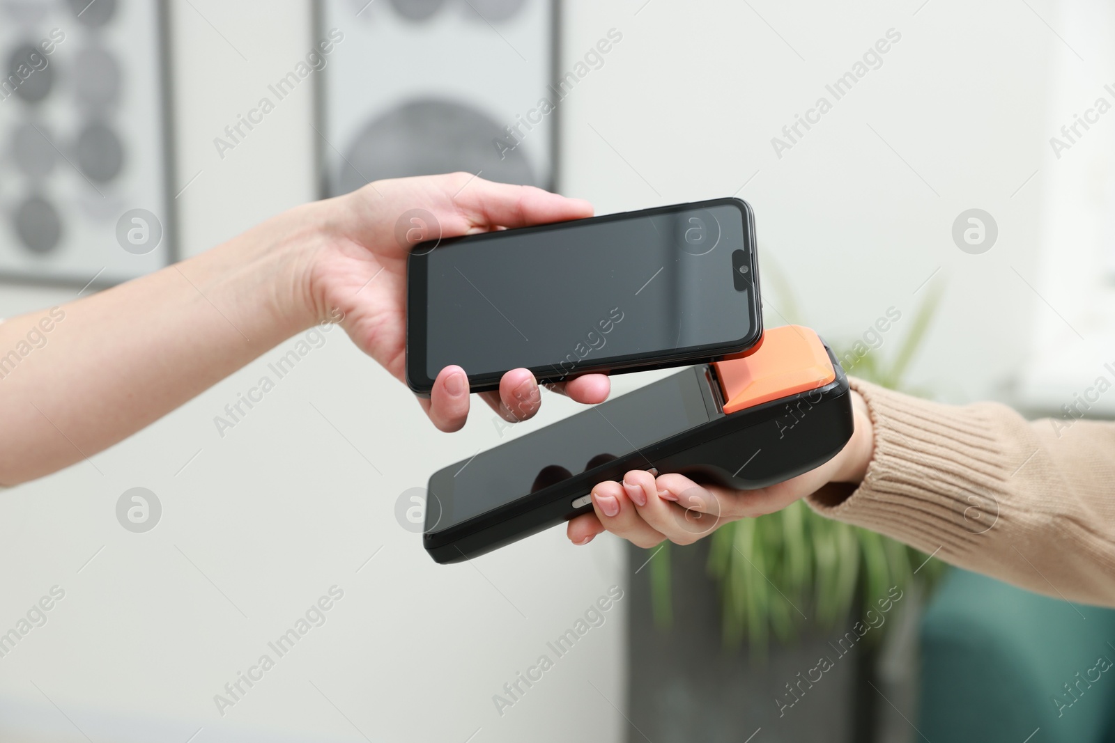 Photo of Woman paying for service with smartphone via terminal indoors, closeup