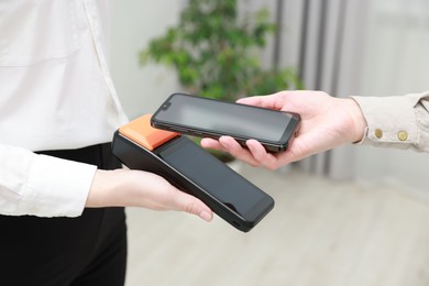 Photo of Woman paying for service with smartphone via terminal indoors, closeup