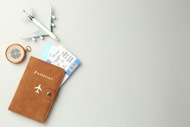 Photo of Passport in brown cover, plane model, compass and flight tickets on light grey background, flat lay. Space for text