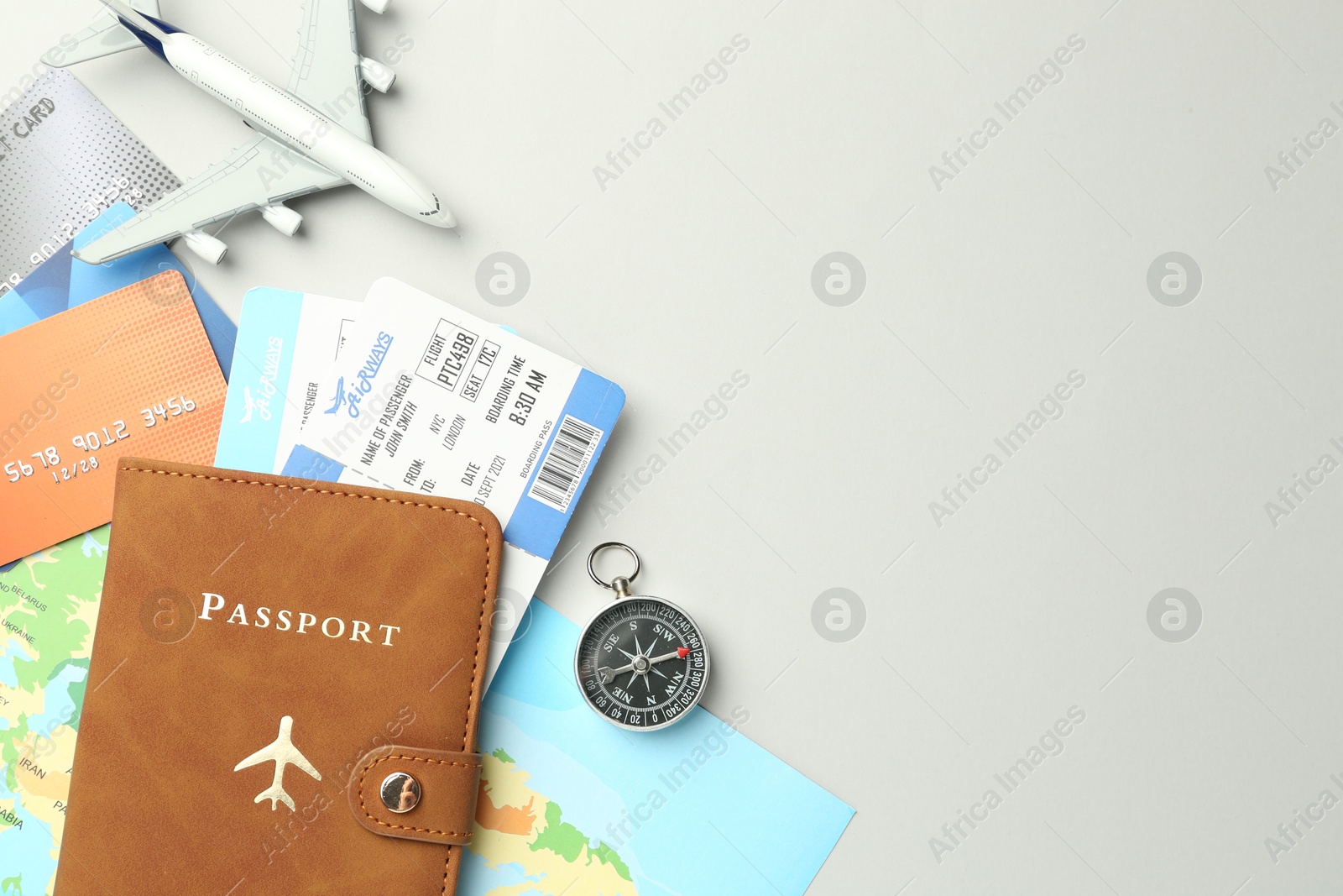 Photo of Passport in brown cover, plane model, compass, credit cards, world map and flight tickets on light grey background, flat lay. Space for text