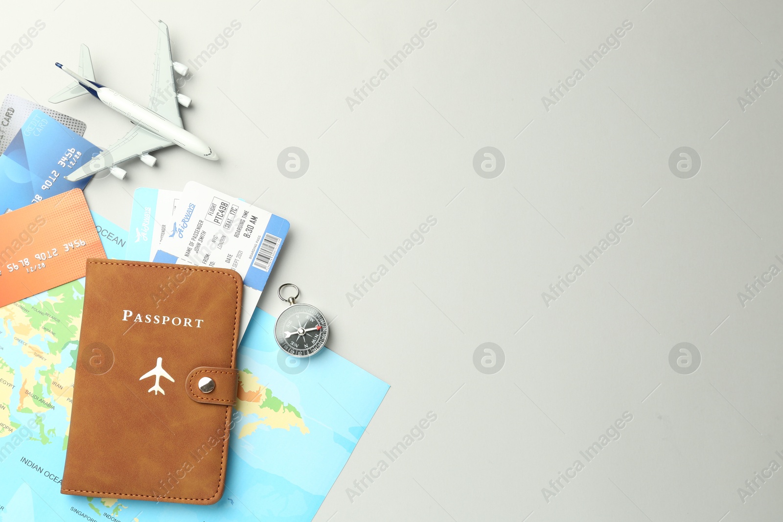 Photo of Passport in brown cover, plane model, compass, credit cards, world map and flight tickets on light grey background, flat lay. Space for text