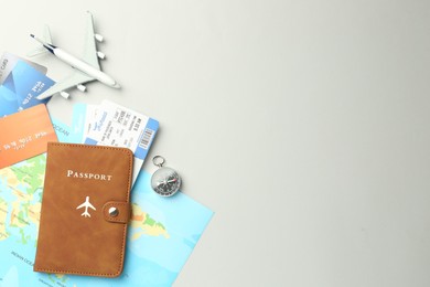 Photo of Passport in brown cover, plane model, compass, credit cards, world map and flight tickets on light grey background, flat lay. Space for text