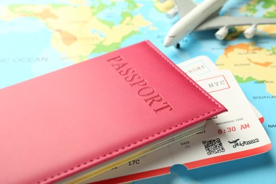 Photo of Passport in pink cover, flight tickets and plane model on world map, closeup