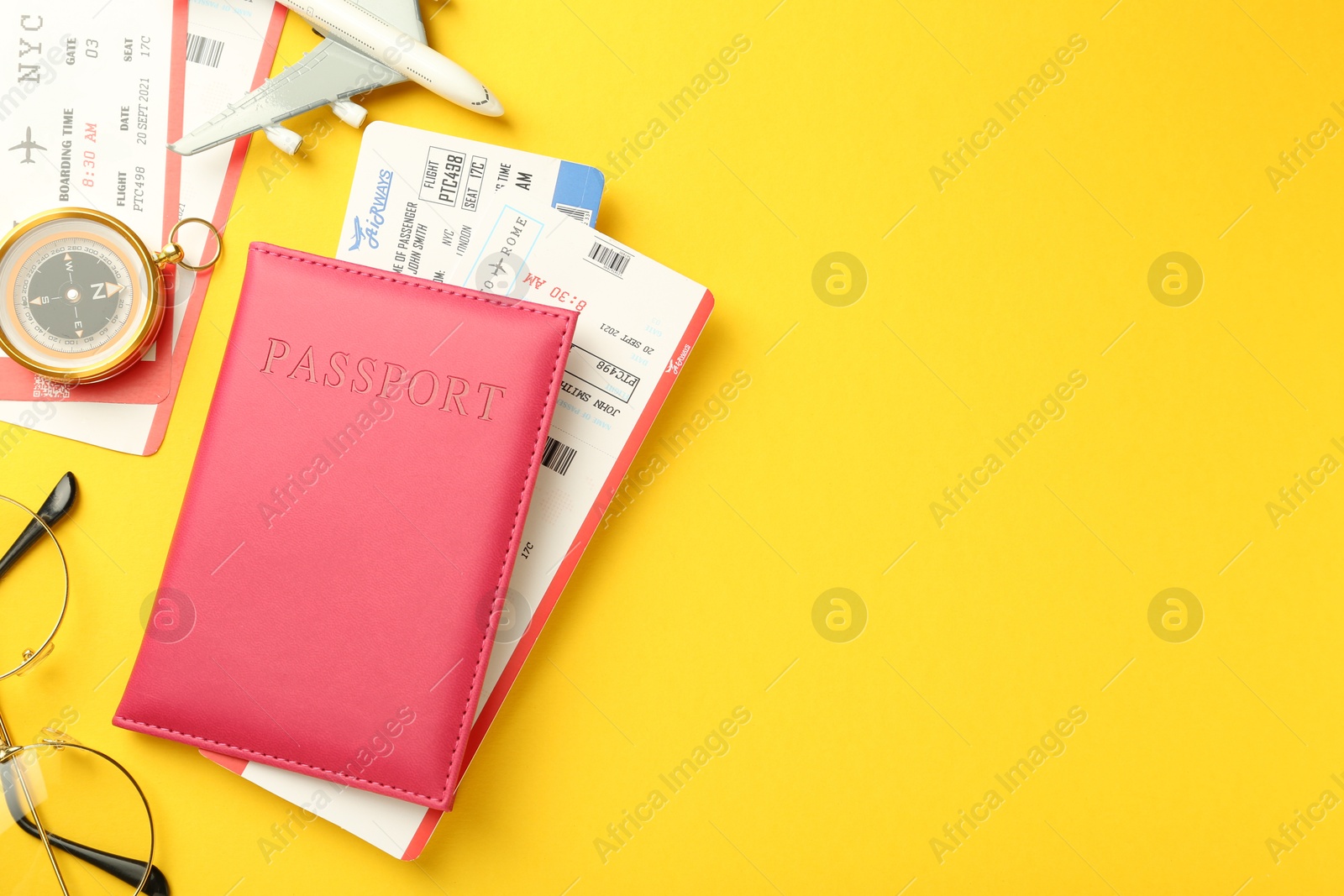 Photo of Passport in pink cover, plane model, compass, glasses and flight tickets on yellow background, flat lay. Space for text