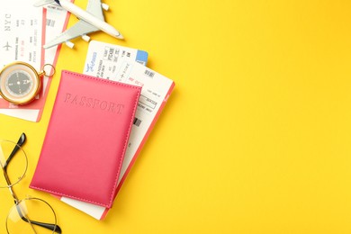 Photo of Passport in pink cover, plane model, compass, glasses and flight tickets on yellow background, flat lay. Space for text