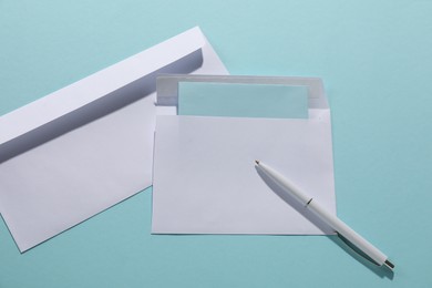 Photo of Paper envelopes with letter and pen on light blue background, flat lay. Mockup for design