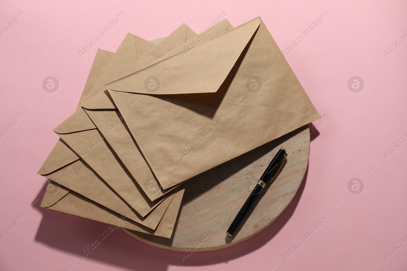 Photo of Kraft paper envelopes and pen on pink background, flat lay. Mockup for design