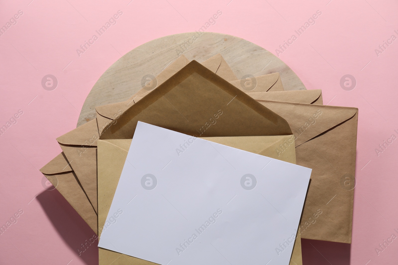 Photo of Kraft paper envelopes and letter on pink background, top view. Mockup for design