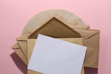 Photo of Kraft paper envelopes and letter on pink background, top view. Mockup for design