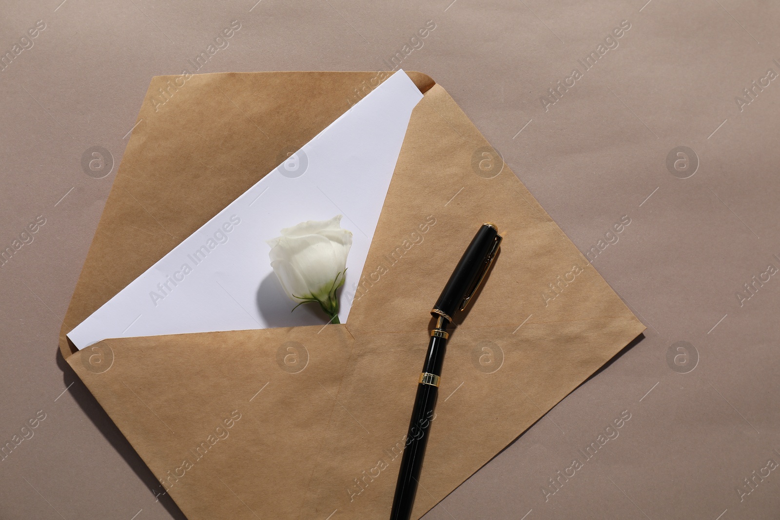 Photo of Kraft paper envelope with letter, flower and fountain pen on dark beige background, top view. Mockup for design