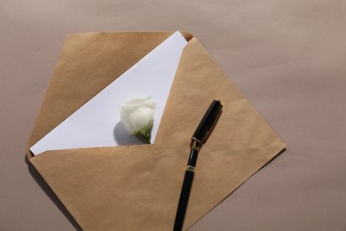 Photo of Kraft paper envelope with letter, flower and fountain pen on dark beige background, top view. Mockup for design