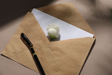 Photo of Kraft paper envelope with letter, flower and fountain pen on dark beige background, top view. Mockup for design