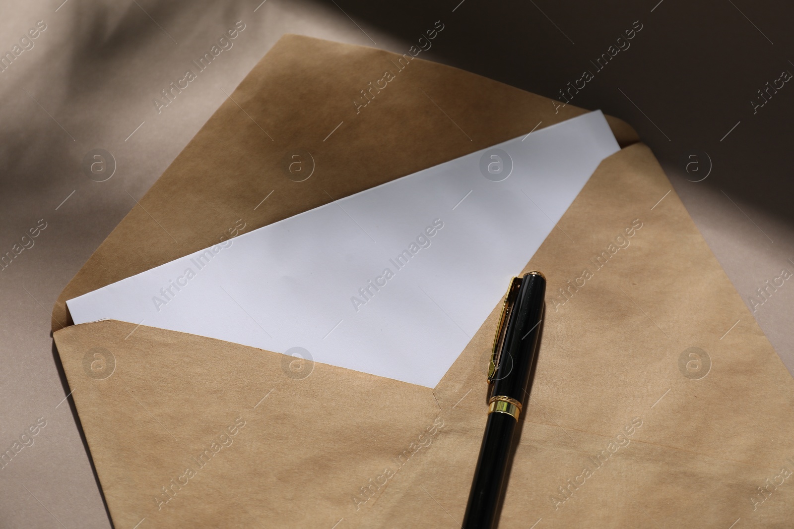 Photo of Kraft paper envelope with letter and fountain pen on dark beige background, above view. Mockup for design