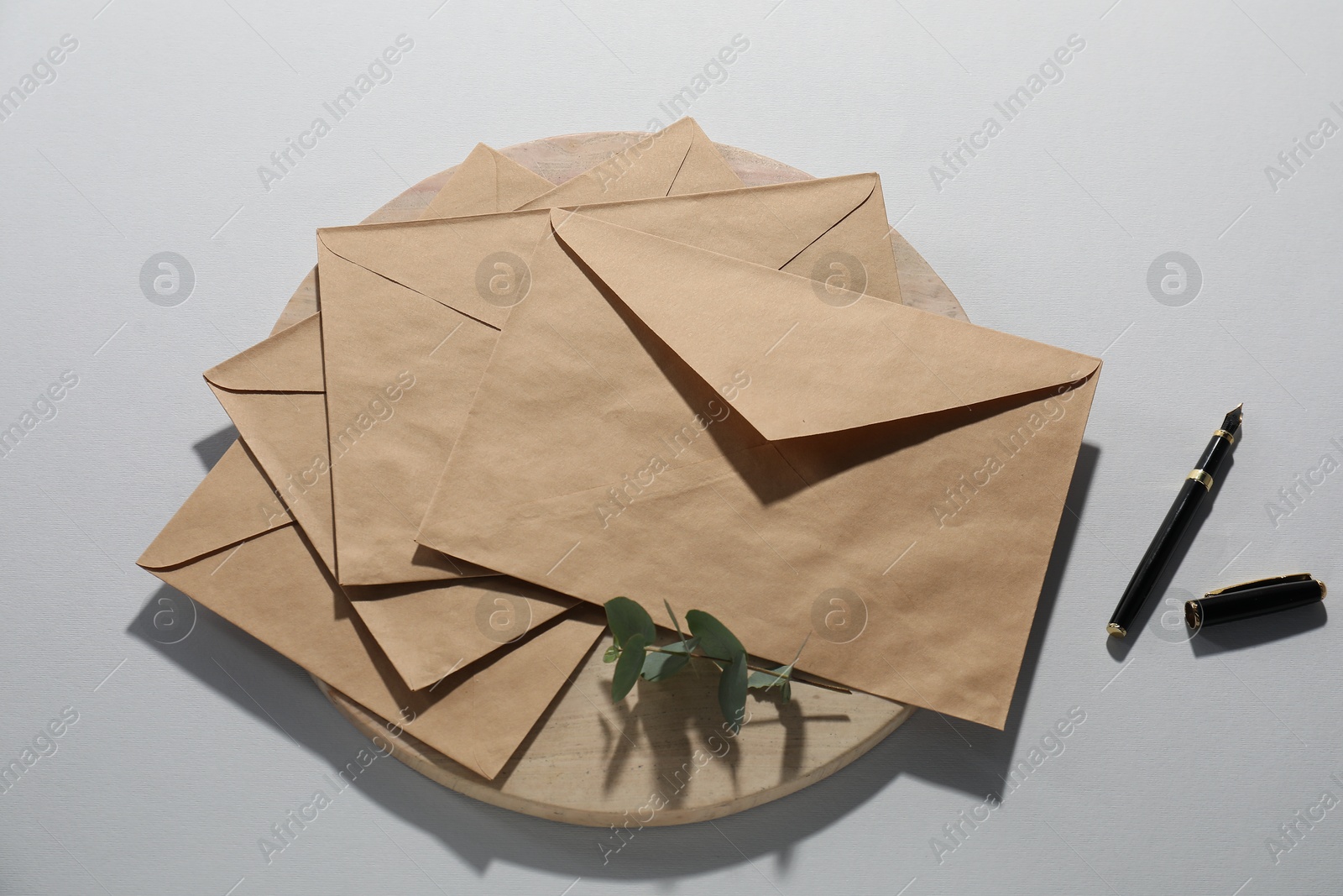 Photo of Kraft paper envelopes, eucalyptus branch and fountain pen on grey background, flat lay. Mockup for design