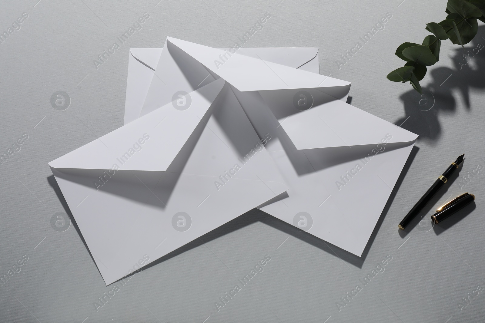 Photo of Paper envelopes, eucalyptus branch and fountain pen on grey background, flat lay. Mockup for design