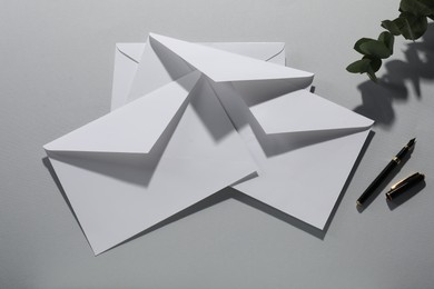 Paper envelopes, eucalyptus branch and fountain pen on grey background, flat lay. Mockup for design