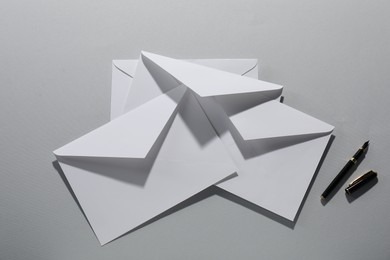 Photo of Paper envelopes and fountain pen on grey background, flat lay. Mockup for design