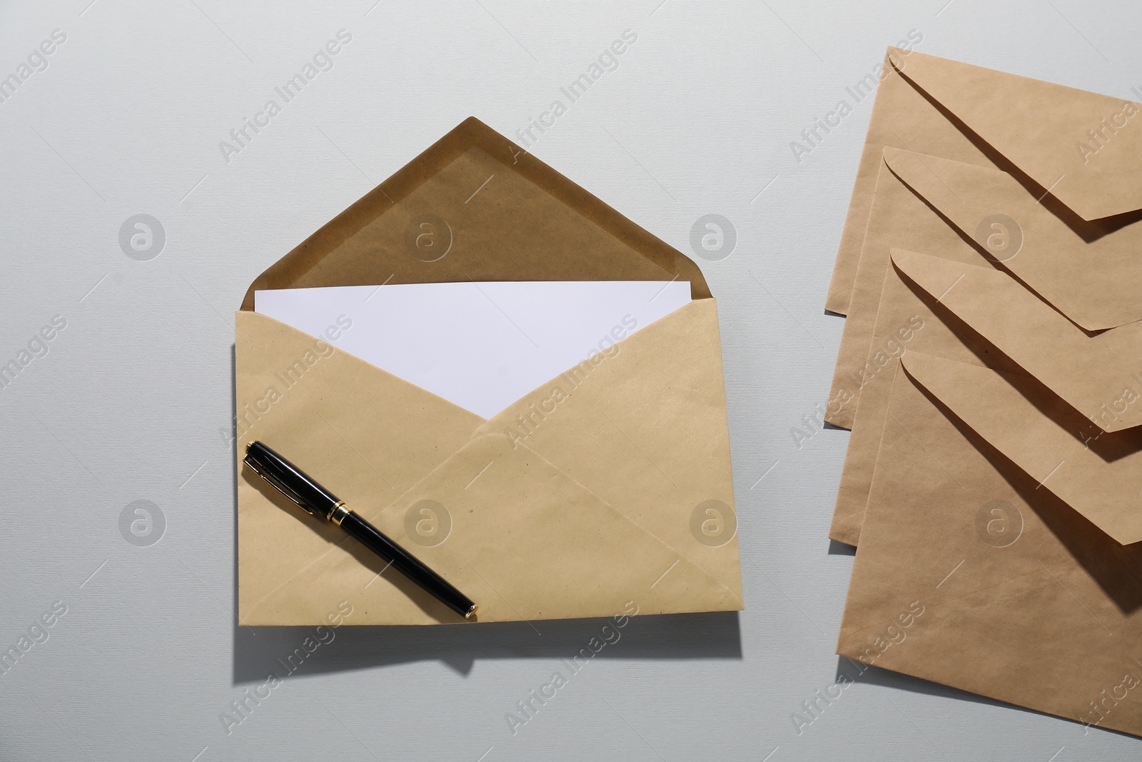 Photo of Kraft paper envelopes with letter and pen on grey background, flat lay. Mockup for design