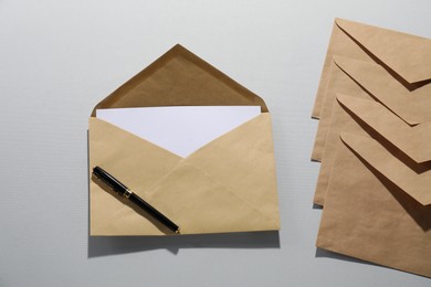 Kraft paper envelopes with letter and pen on grey background, flat lay. Mockup for design