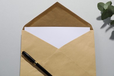 Photo of Kraft paper envelope with letter, pen and eucalyptus branch on grey background, above view. Mockup for design