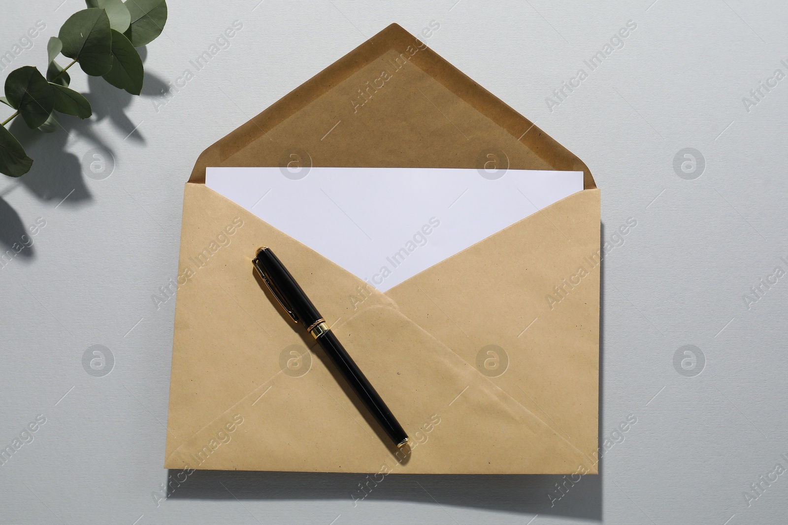 Photo of Kraft paper envelope with letter, pen and eucalyptus branch on grey background, top view. Mockup for design