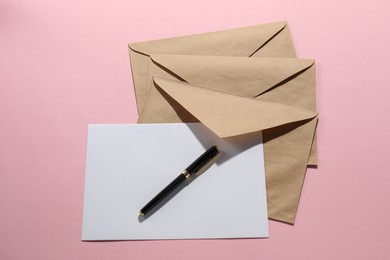 Photo of Kraft paper envelopes with letter and pen on pink background, flat lay. Mockup for design