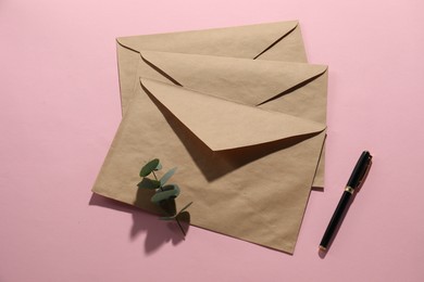 Photo of Kraft paper envelopes, eucalyptus branch and pen on pink background, flat lay. Mockup for design