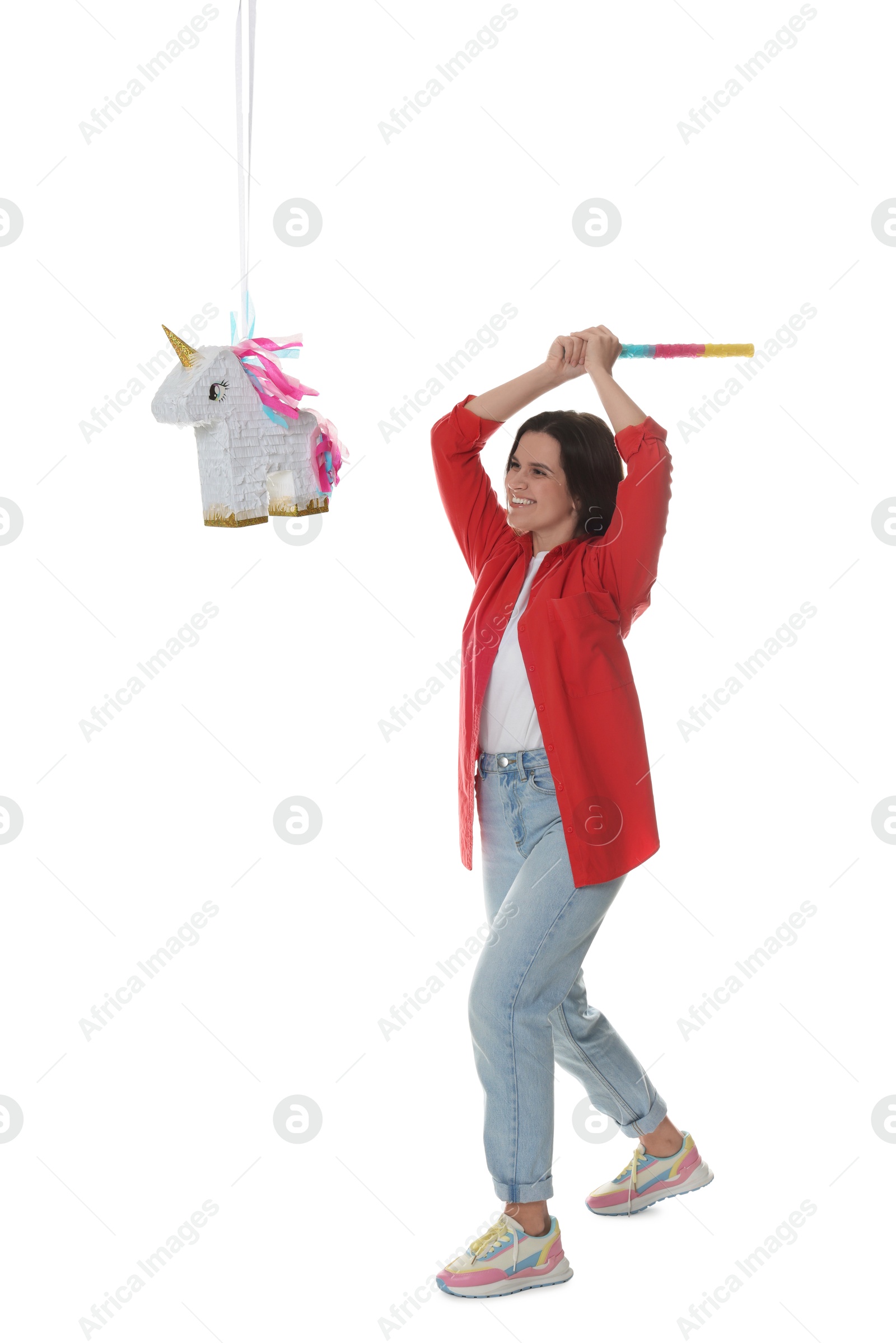 Photo of Happy woman hitting unicorn shaped pinata with stick on white background