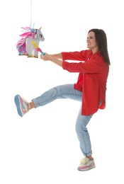 Photo of Happy woman hitting unicorn shaped pinata with stick on white background