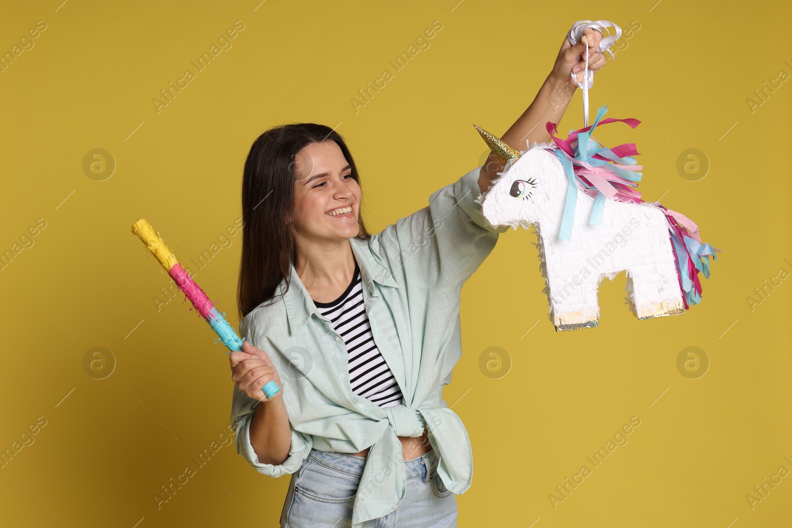 Photo of Happy woman with unicorn shaped pinata and stick on yellow background