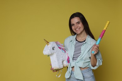 Photo of Happy woman with unicorn shaped pinata and stick on yellow background, space for text