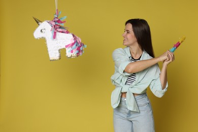 Photo of Happy woman hitting unicorn shaped pinata with stick on yellow background