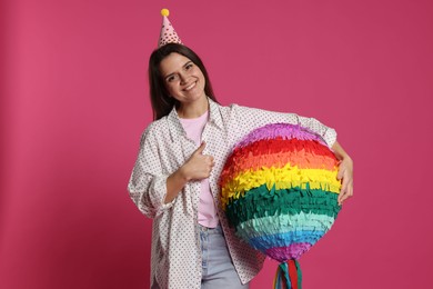 Photo of Happy woman with colorful pinata showing thumbs up on pink background