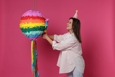 Photo of Happy woman hitting colorful pinata with stick on pink background