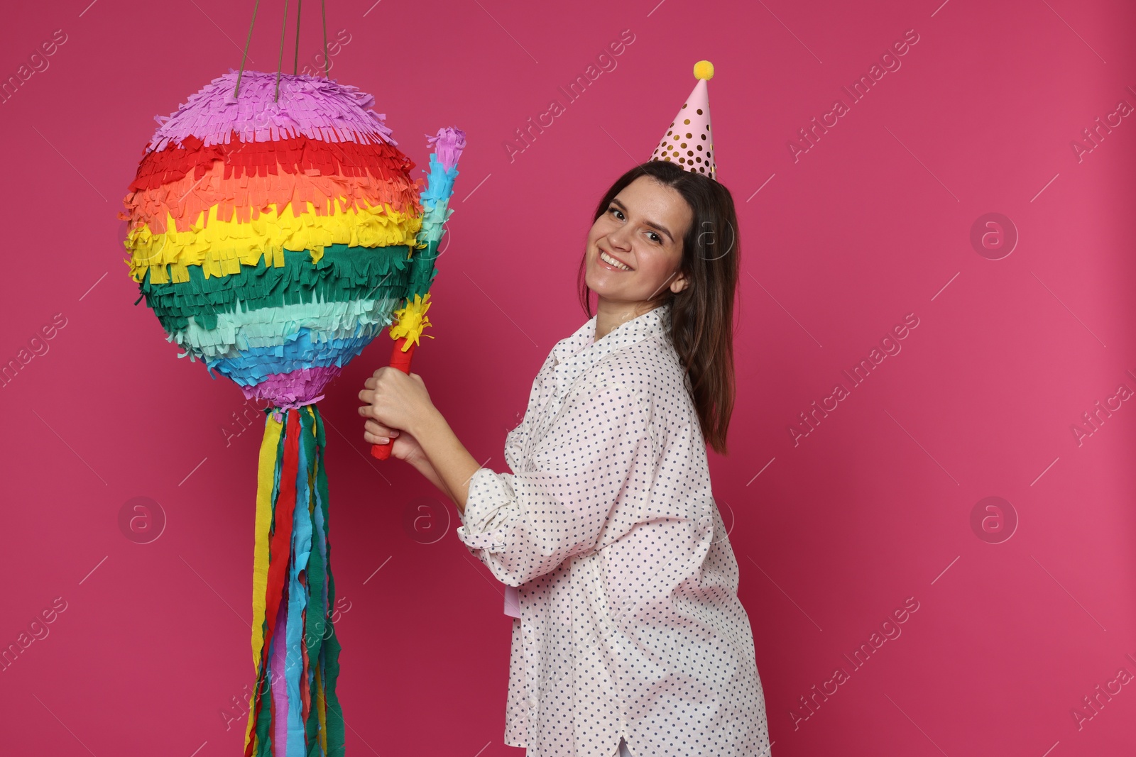 Photo of Happy woman with colorful pinata and stick on pink background