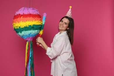 Photo of Happy woman with colorful pinata and stick on pink background