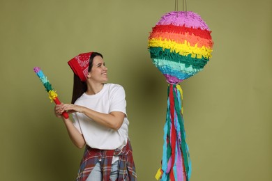 Photo of Happy woman hitting colorful pinata with stick on green background