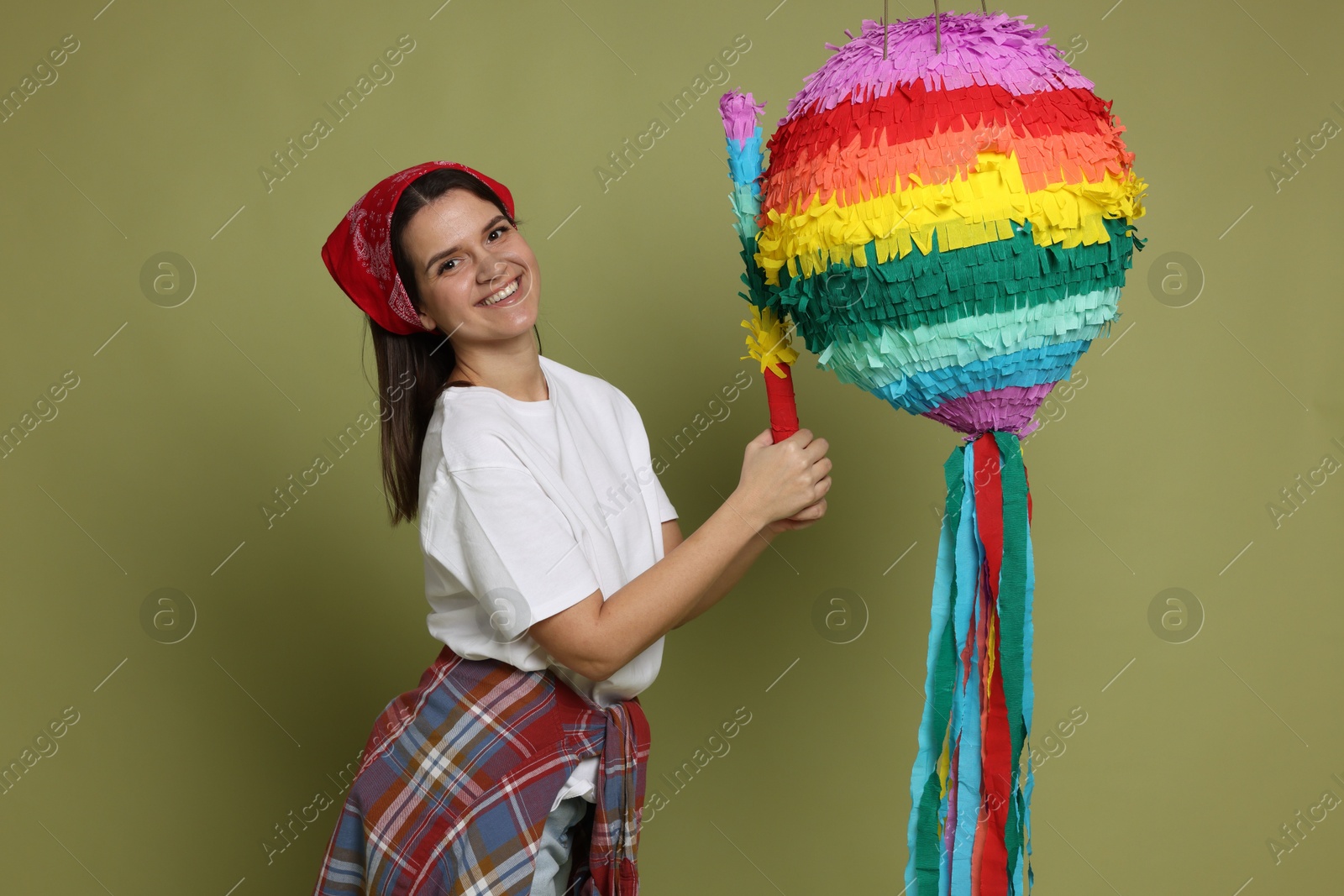 Photo of Happy woman hitting colorful pinata with stick on green background