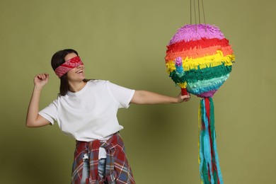 Photo of Woman with tied eyes breaking pinata on green background