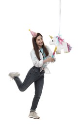 Happy woman hitting unicorn shaped pinata with stick on white background