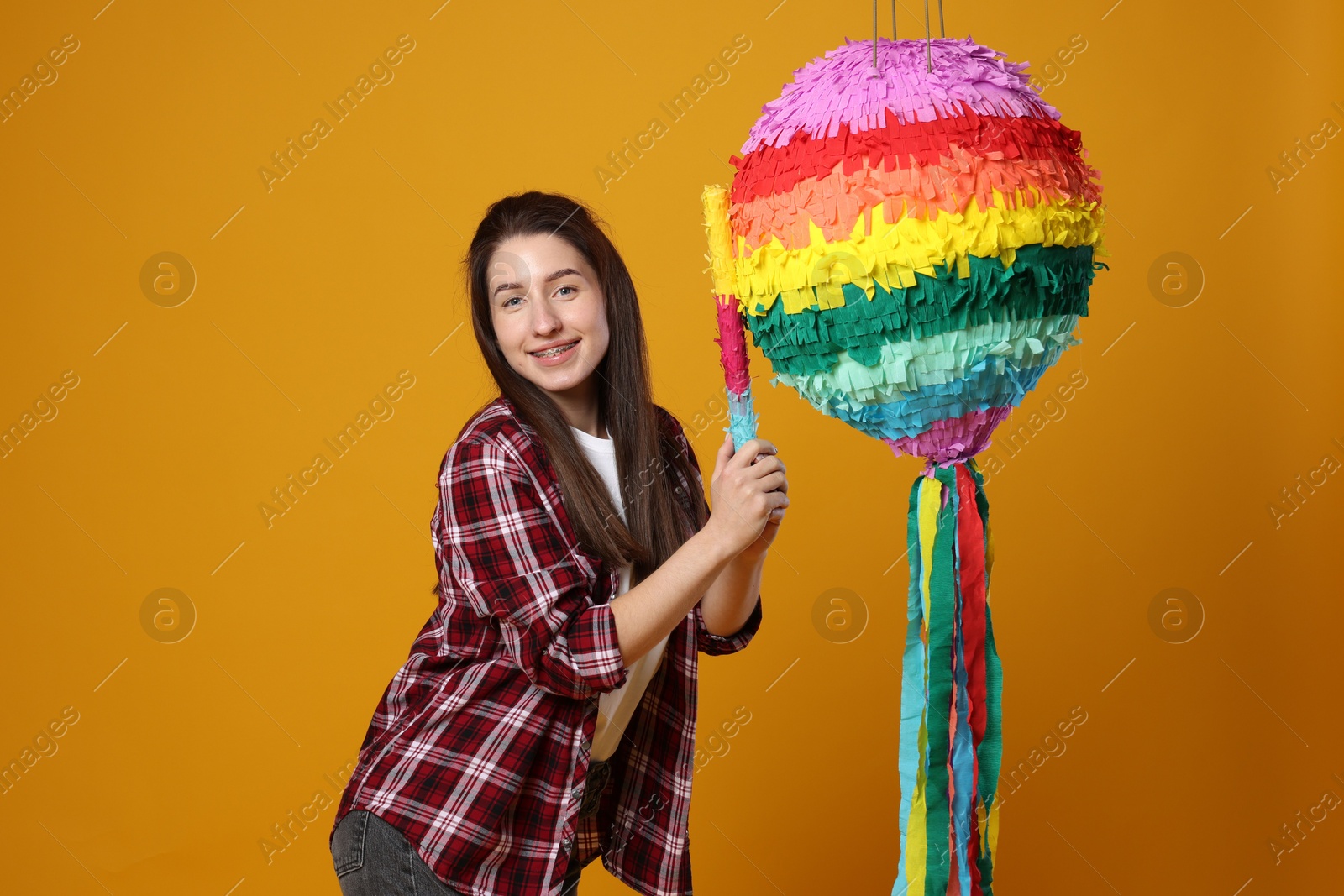 Photo of Happy woman hitting colorful pinata with stick on orange background