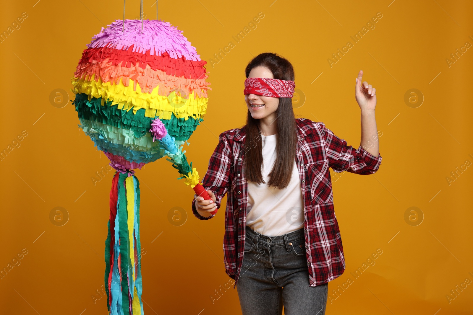 Photo of Woman with tied eyes breaking pinata on orange background