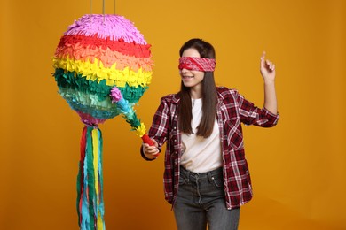 Photo of Woman with tied eyes breaking pinata on orange background